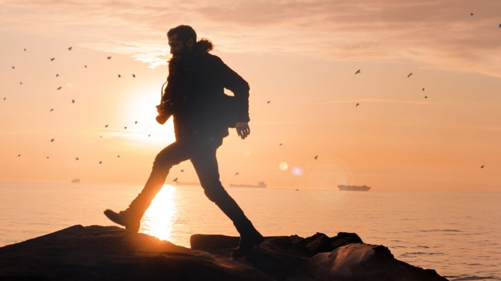 A silhouette of a man walking on rocks by the sea at sunset, evoking wanderlust.