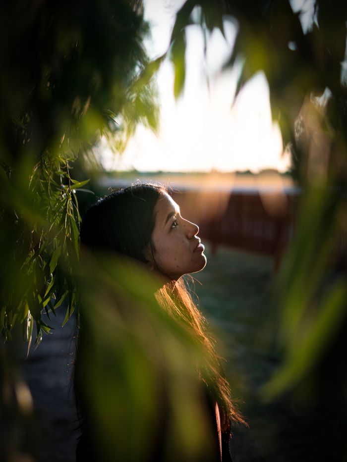 A woman gazes thoughtfully among leaves, bathed in warm, soft lighting.