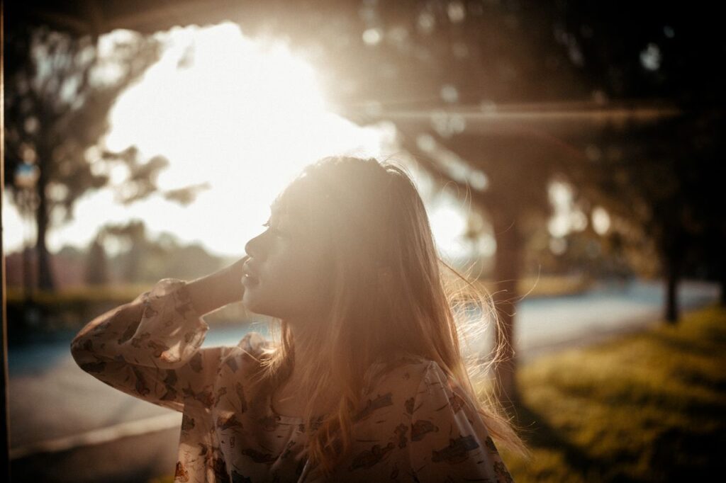 A woman with flowing hair enjoys the sunlight during golden hour outdoors.
